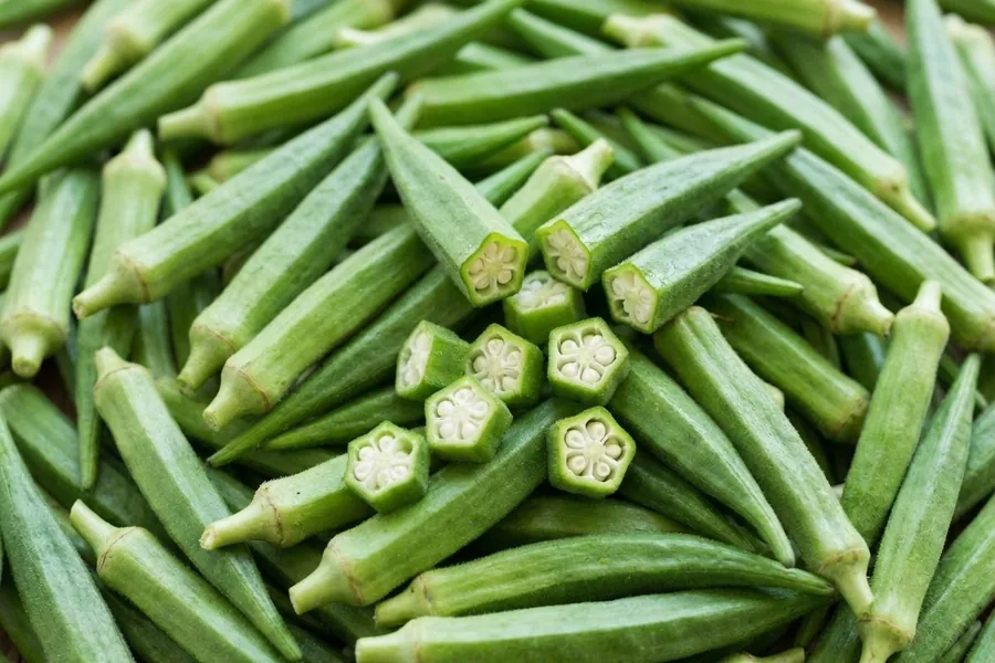 Fresh okra pods filling the frame, with short cut pieces in the middle showing the five-sided seed section